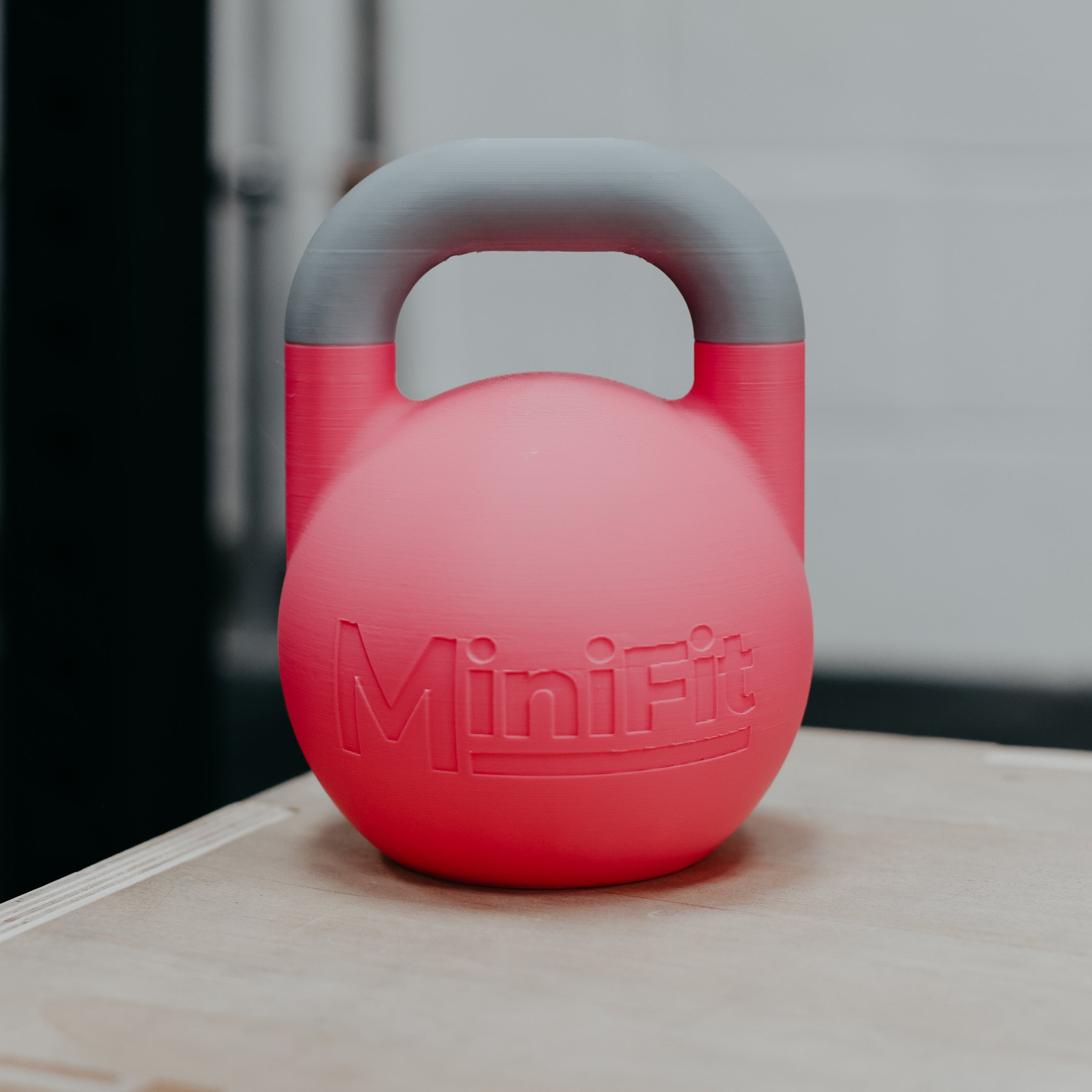 Pink children's kettlebell with grey handle on a wooden surface, featuring the MiniFit brand.