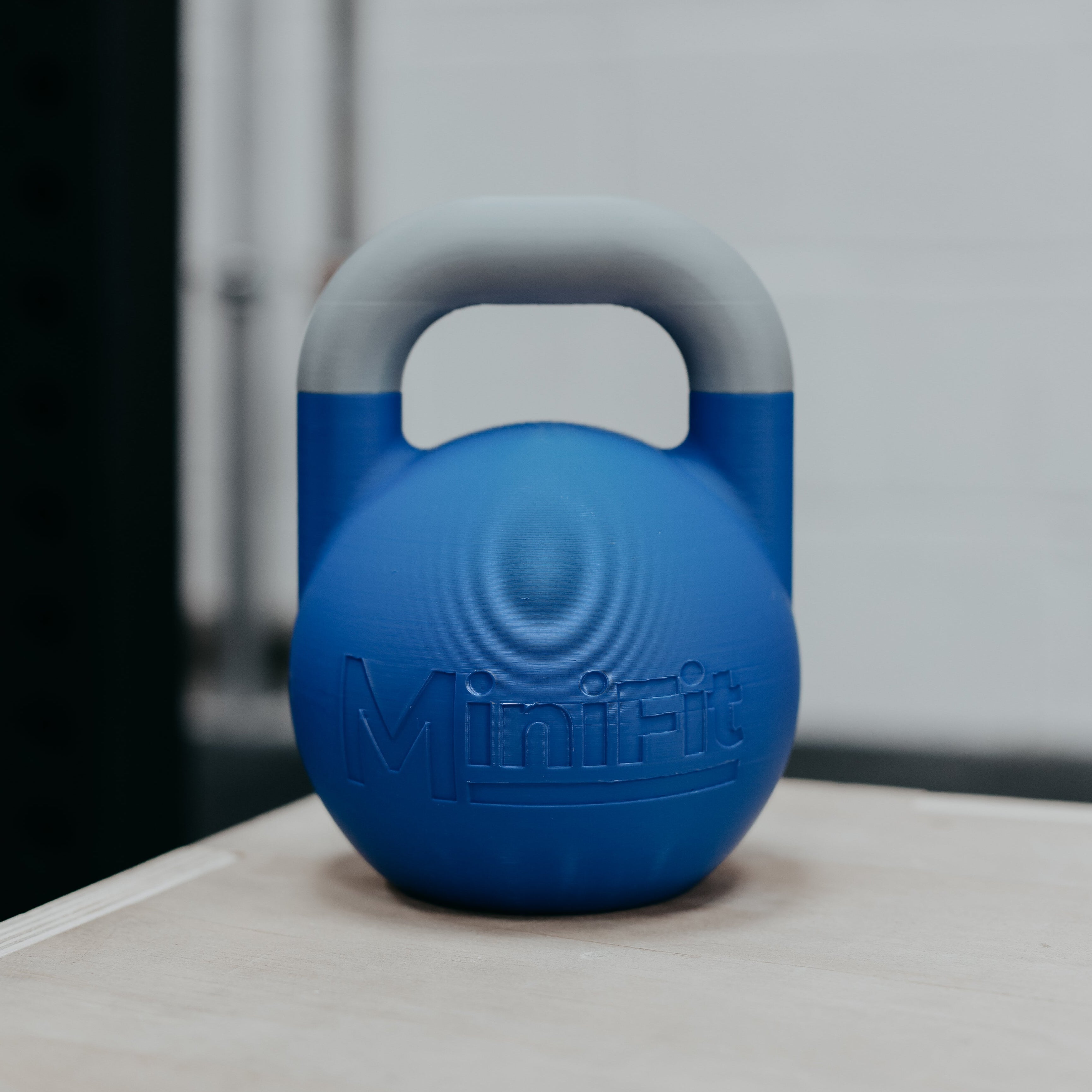 Blue mini kids fitness kettlebell weight with MiniFit branding on a wooden surface.