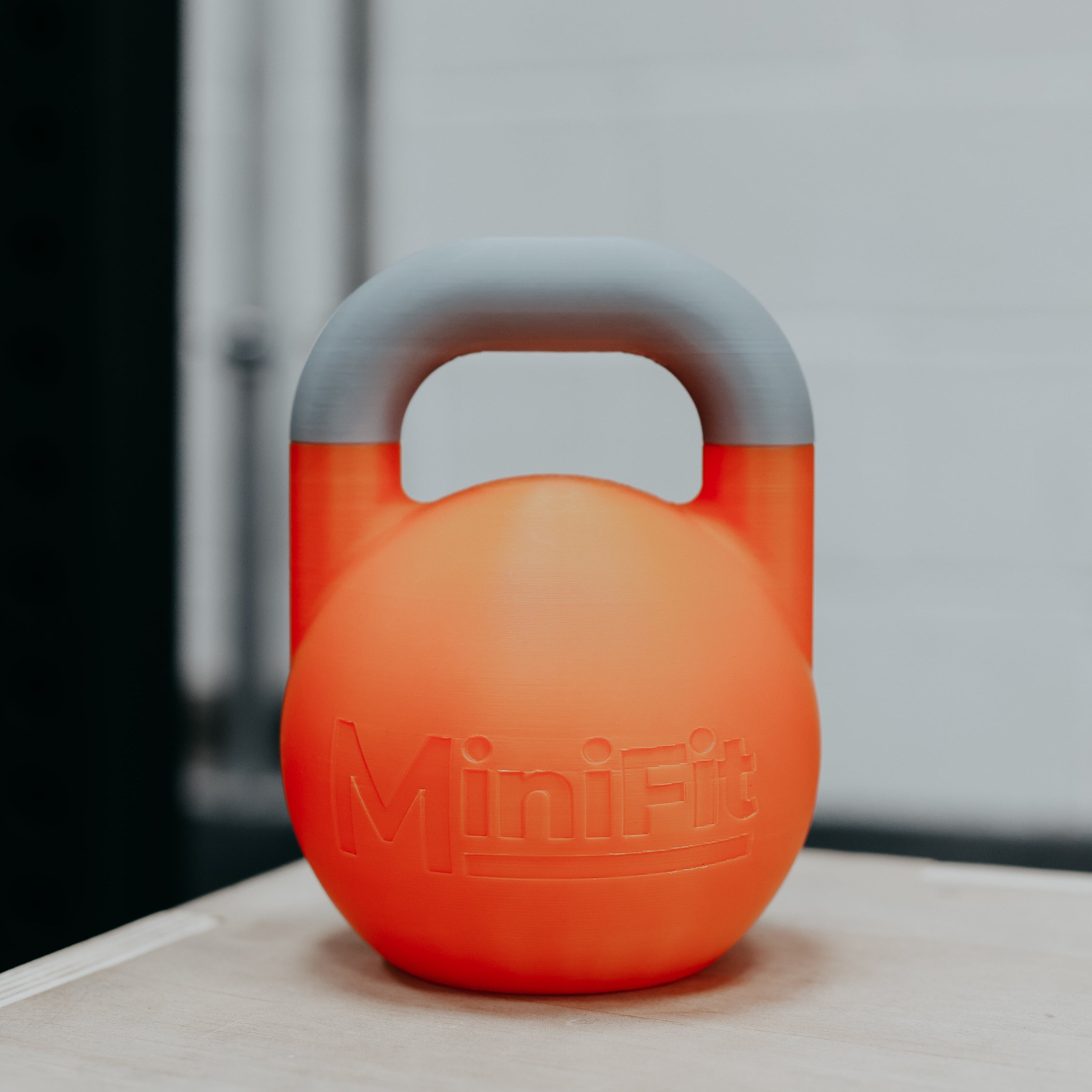 Orange children's kettlebell with grey handle on a light surface