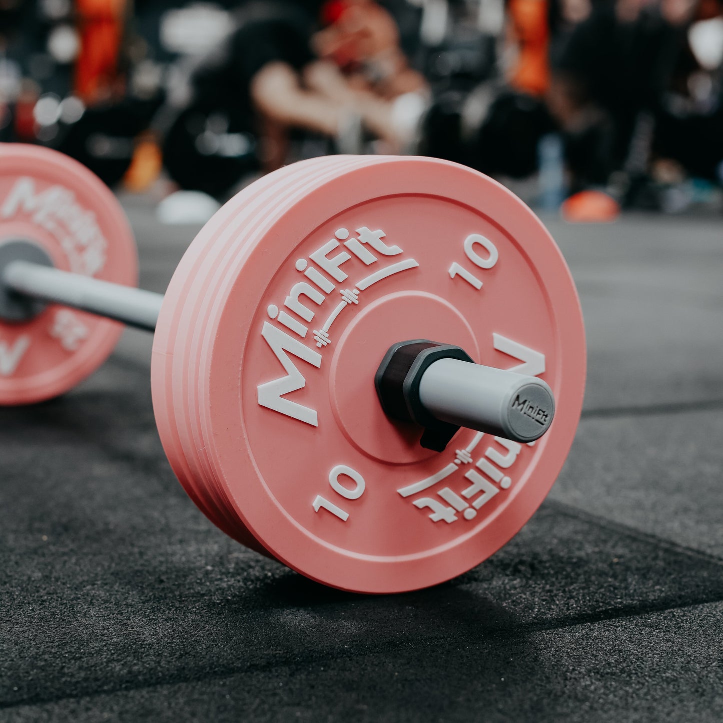 Pink weight plate with 'MiniFit' branding on a gym floor.