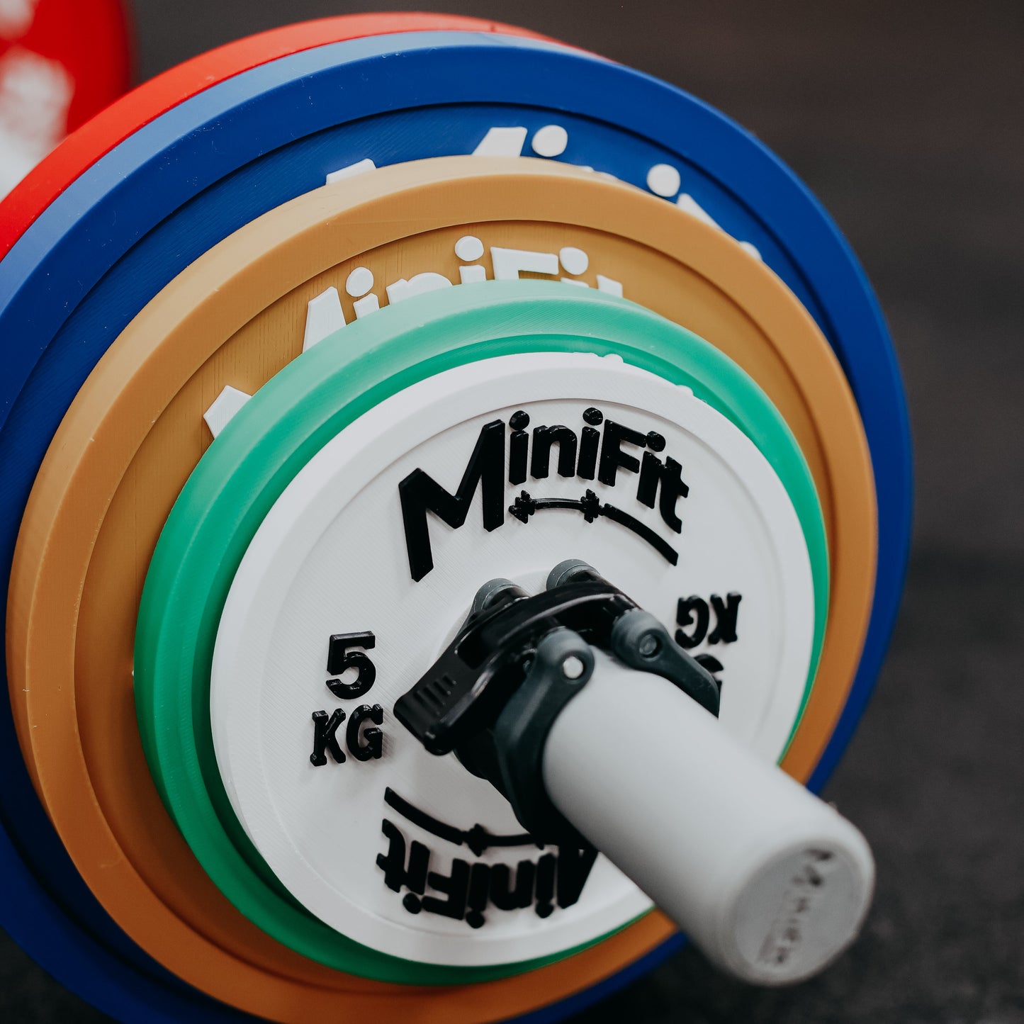Colorful kids barbell loaded with powerlifting plates with 'Minifit' branding on a gym background