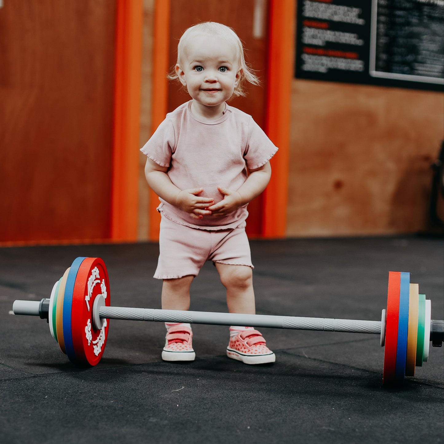 Child standing next to a colorful kids barbell set in a gym setting