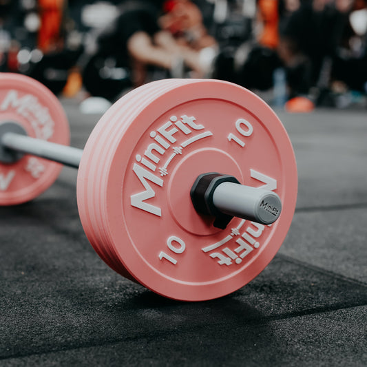 Pink weight plate with 'MiniFit' branding on a gym floor.