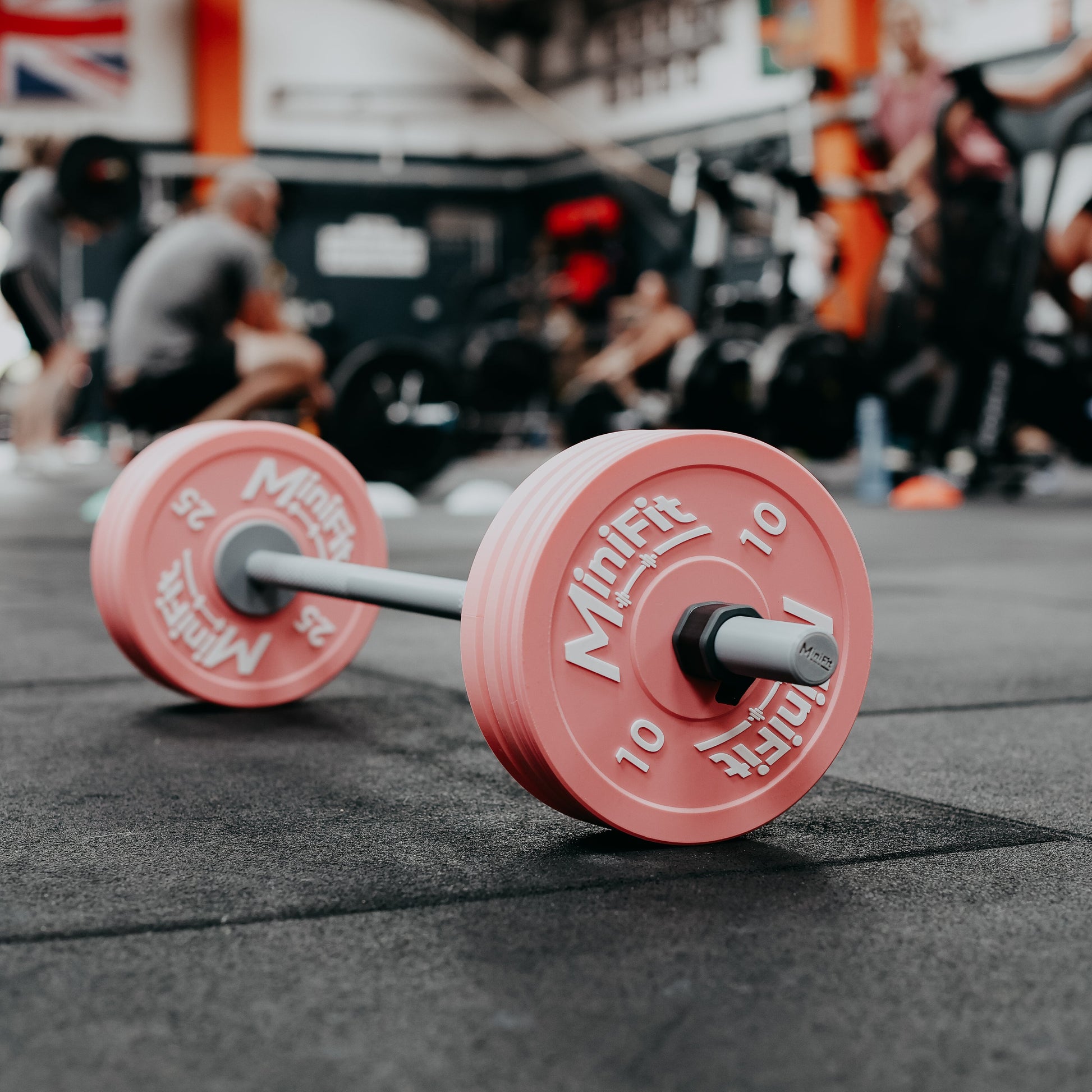 Pink barbell with weights on a gym floor, people in the background