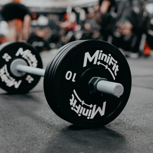 black kids bumper plates on a barbell with 'Minifit' branding on a gym floor.