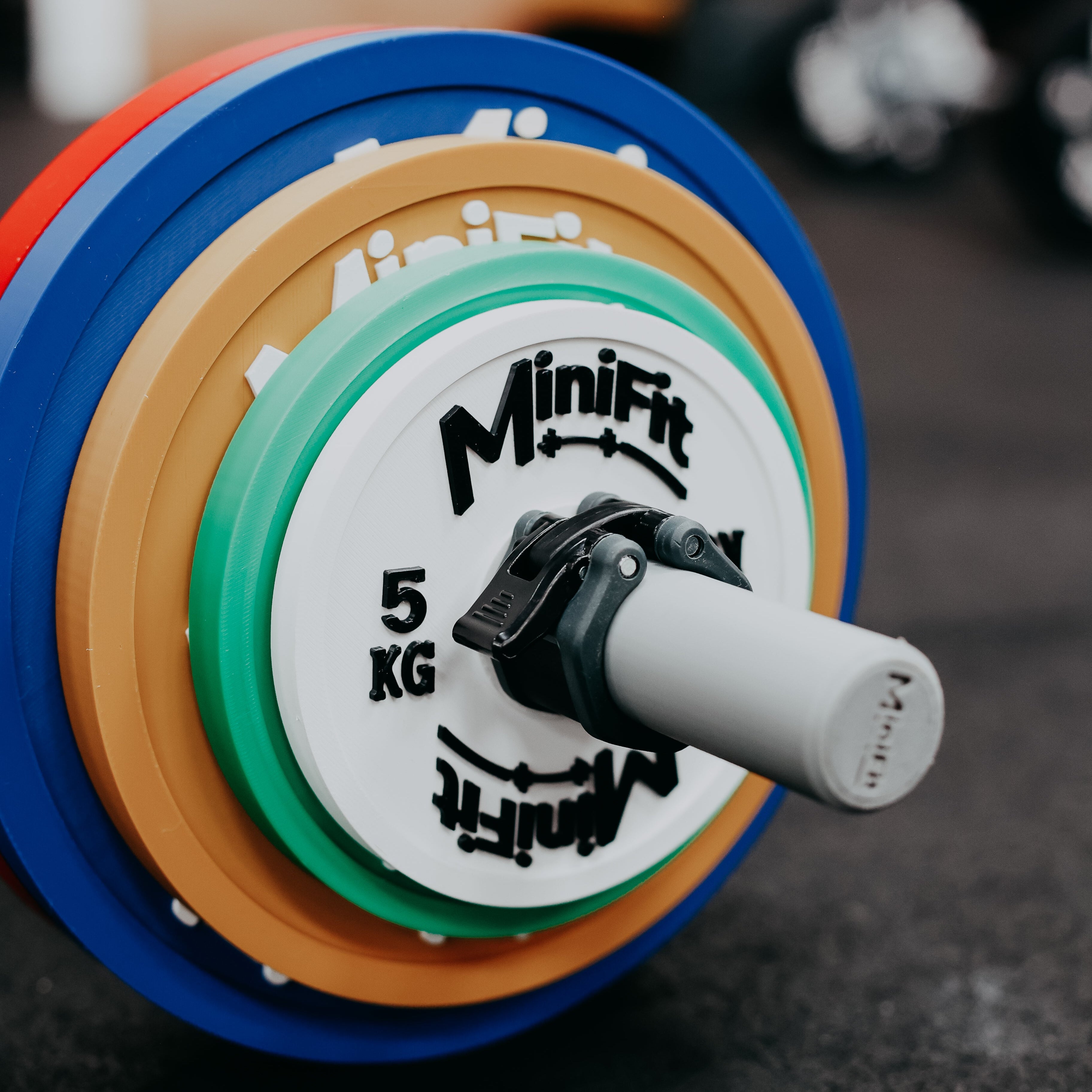 Colourful powerlifting children's weight plate with Minifit branding on a gym background