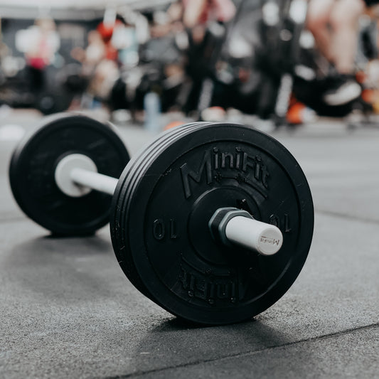 kids Barbell with black weight plates on a gym floor, background of people exercising