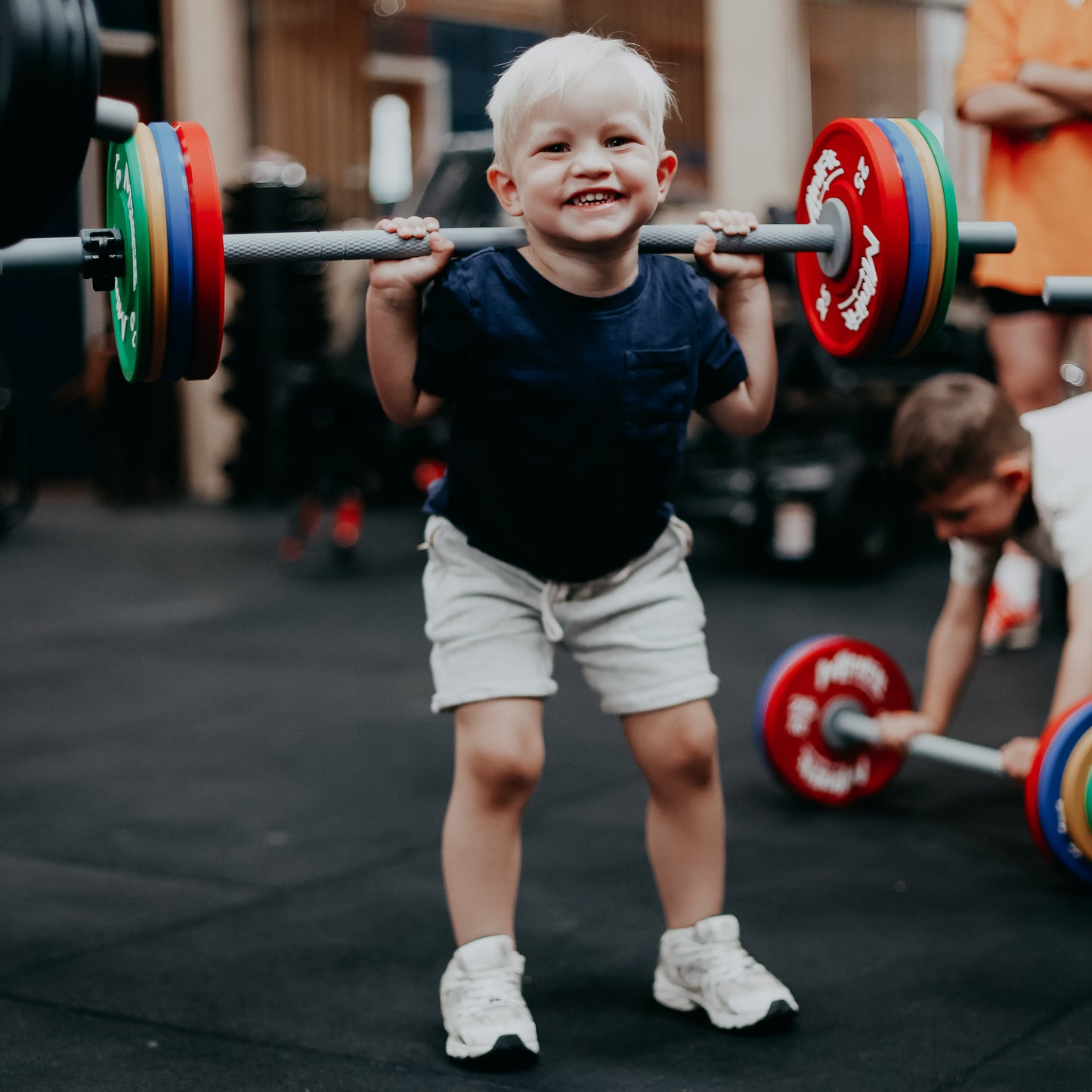 Child lifting a barbell with colourful weights in a gym setting