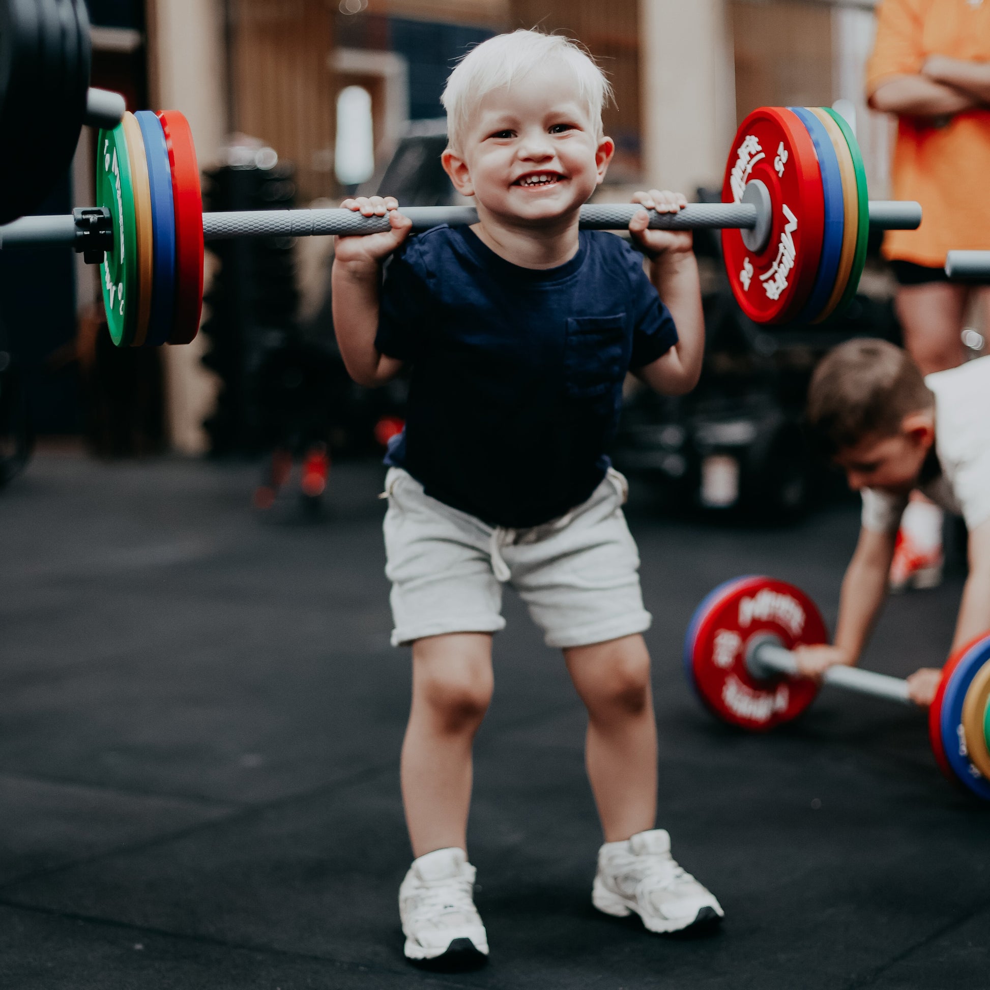 Child lifting a barbell with colourful weights in a gym setting