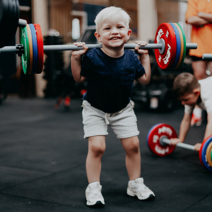 Child lifting a barbell with colourful weights in a gym setting