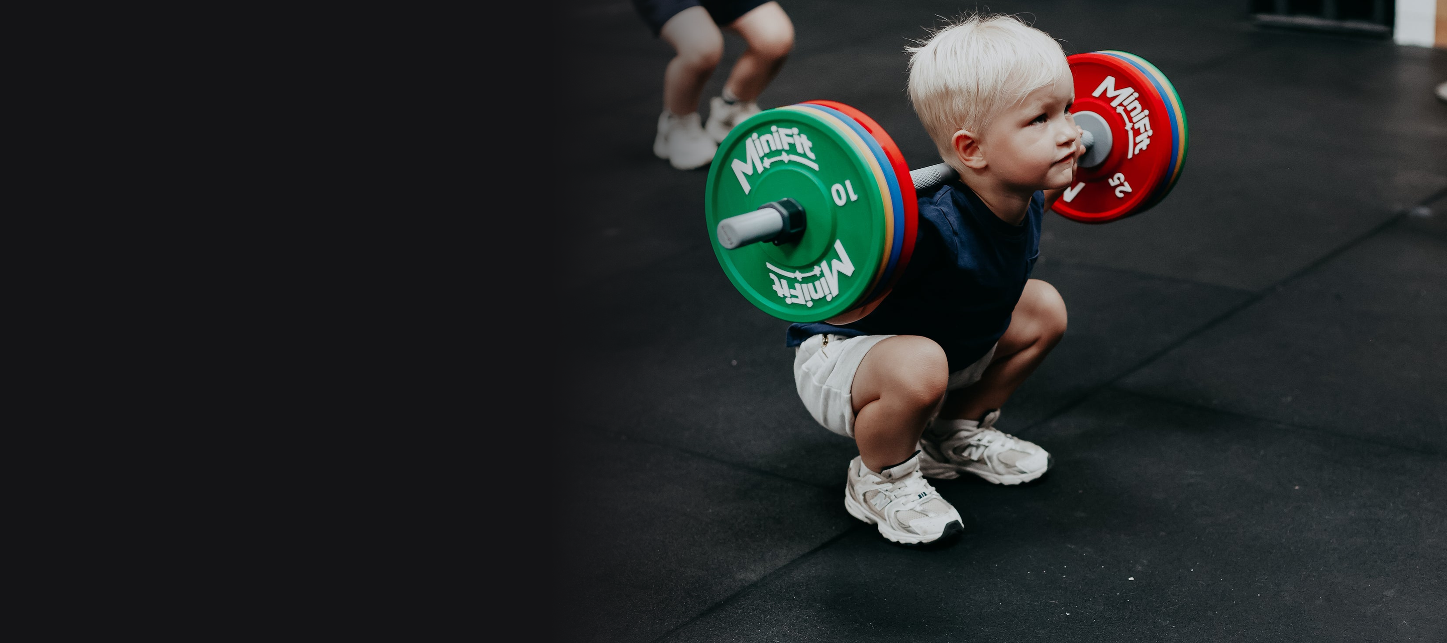 Child in a supervised class squatting with an unloaded-weight MiniFit Play barbell, dark panel left for text