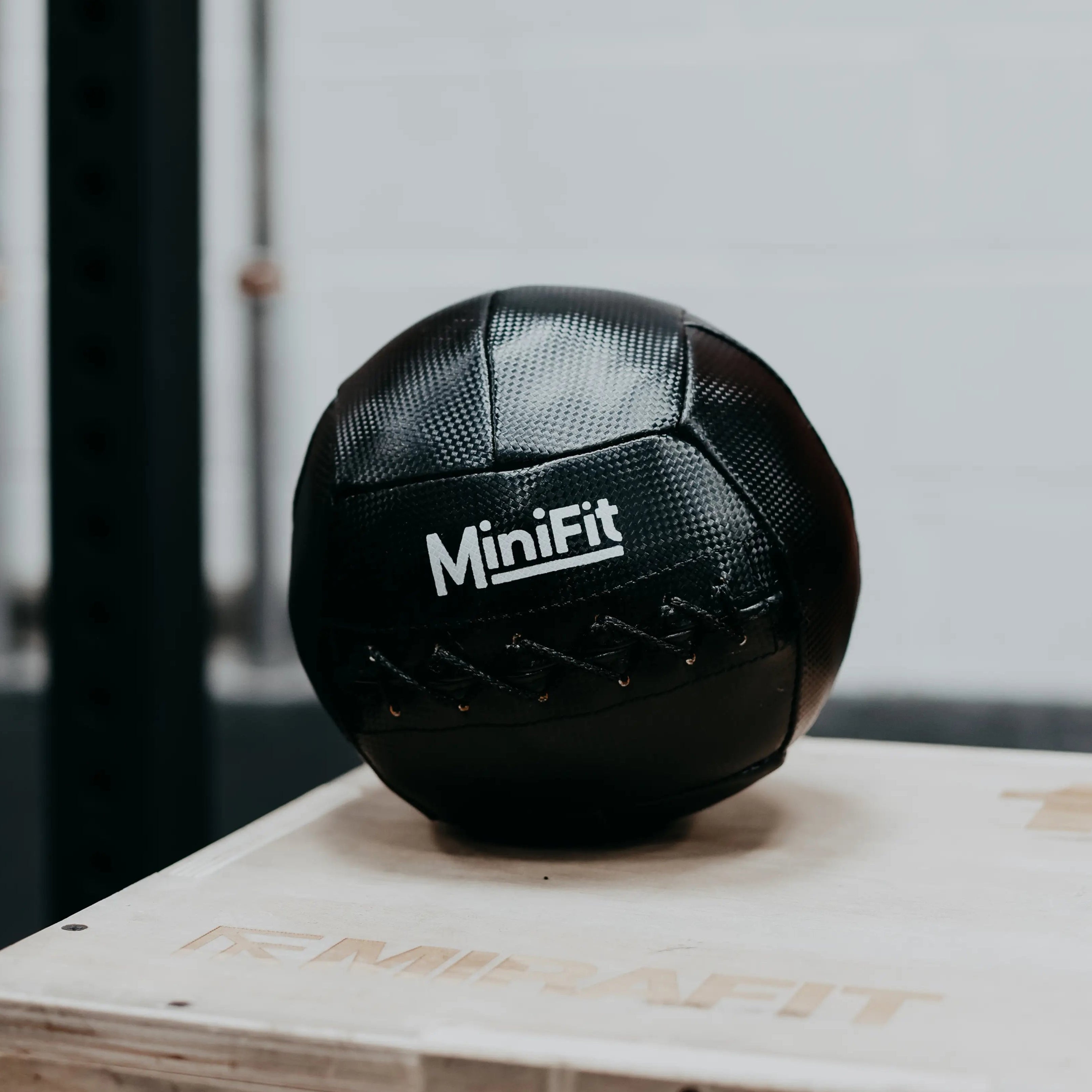 Black MiniFit exercise ball on a wooden box with a blurred background. Mini kids Wallball, made for children.