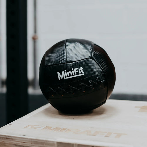 Black MiniFit exercise ball on a wooden box with a blurred background. Mini kids Wallball, made for children.
